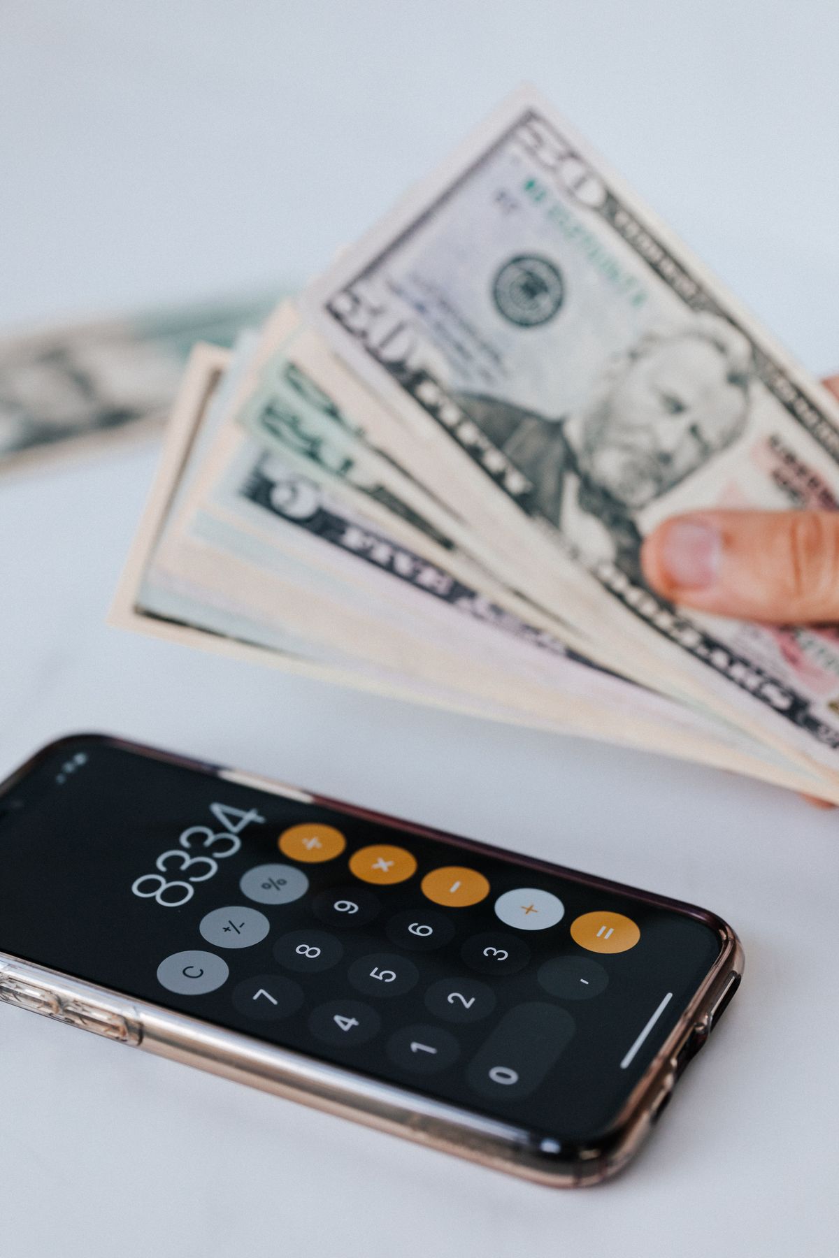 Person using a smartphone calculator while holding banknotes