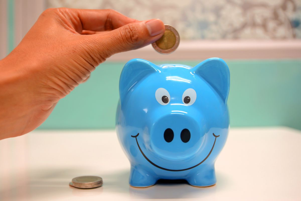 Hand placing a coin into a blue piggy bank