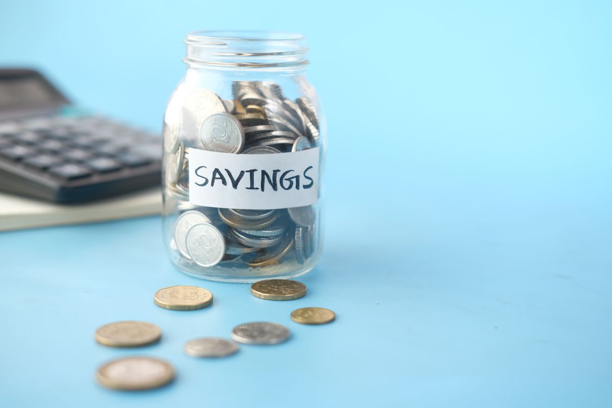 Savings jar filled with coins beside a calculator